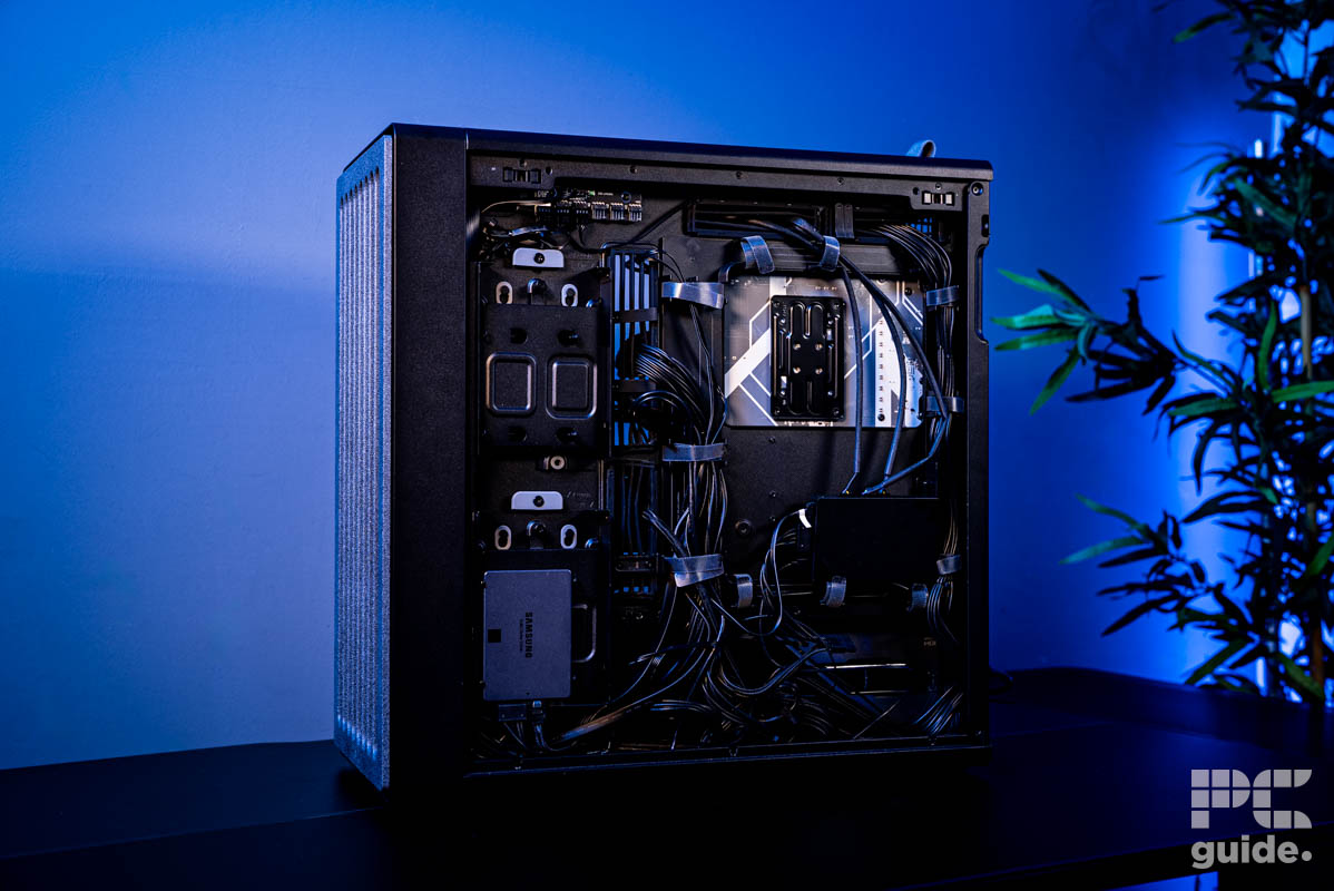 The left side of the HAVN BF 360 Flow case with all the cables routed to the various places with an SSD mounted in the bottom left. Ther is a plnat to the right and a blue painted wall behind.