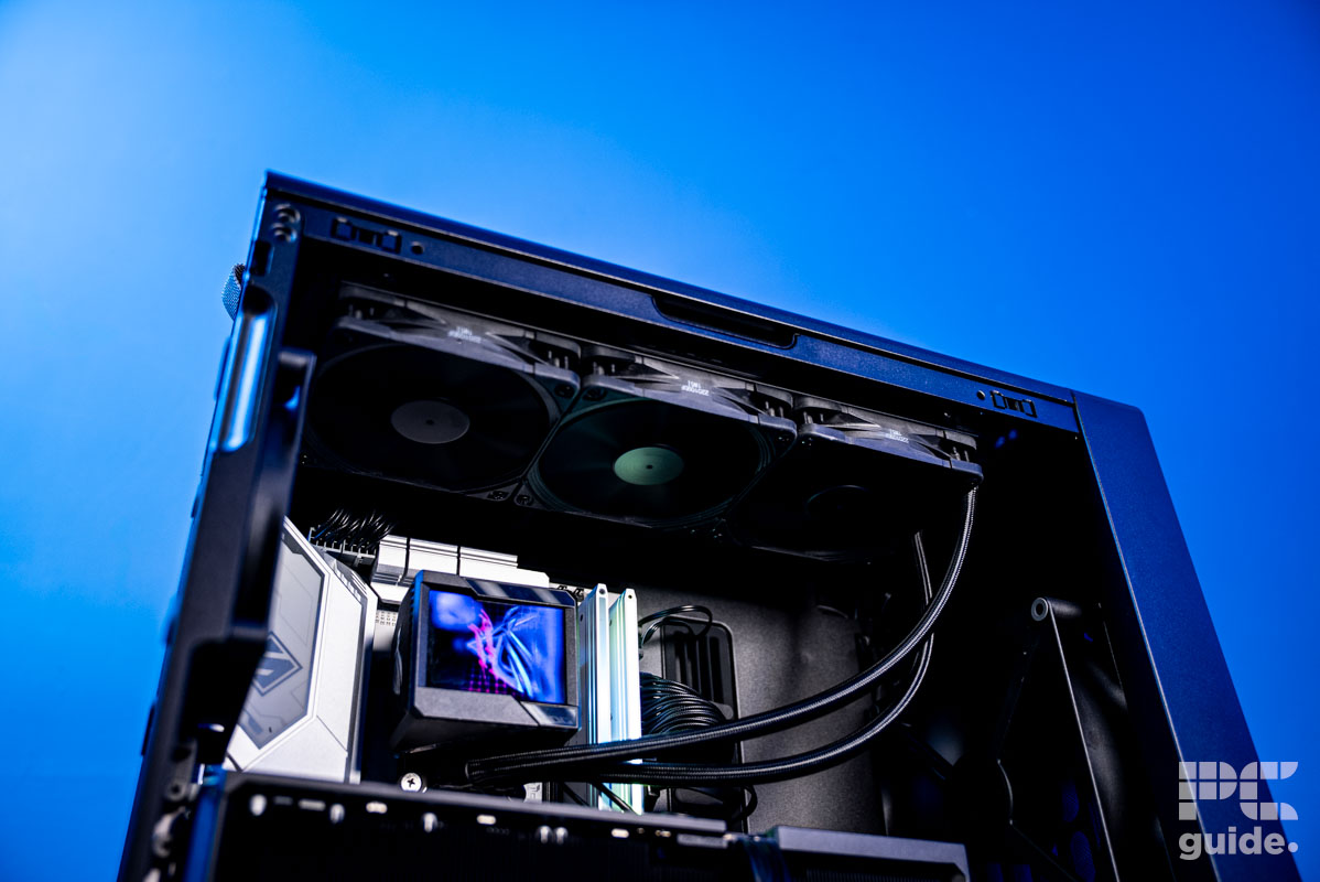 The HAVN BF 360 Flow case insdie lookign up at the three fans on the radiator attacched to the top. Below are the motherboard, AIO, and GPU, with a background of a blue wall.