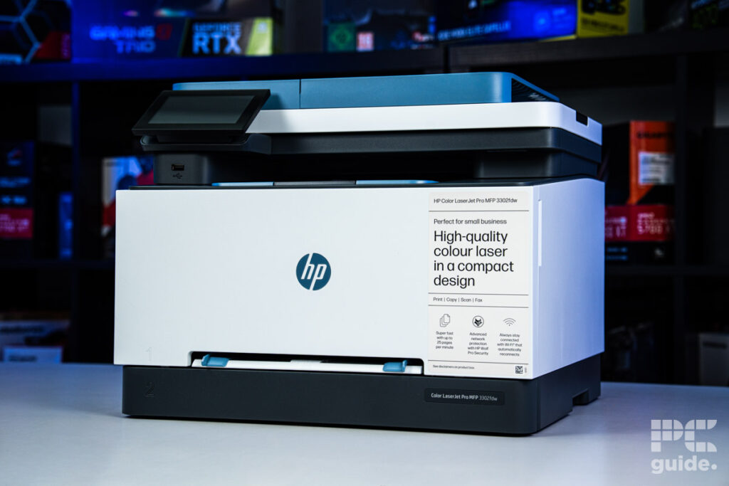 The front of the HP Color LaserJet 3302fdw. Sitting on a white table, with a background of a bookshelf filled with PC component boxes.