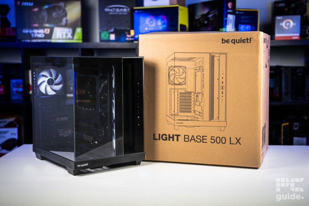 The be quiet! Light Base 500 LX standing next to its brown box. Standing on a white table with a background of a pc components on a bookshelf.